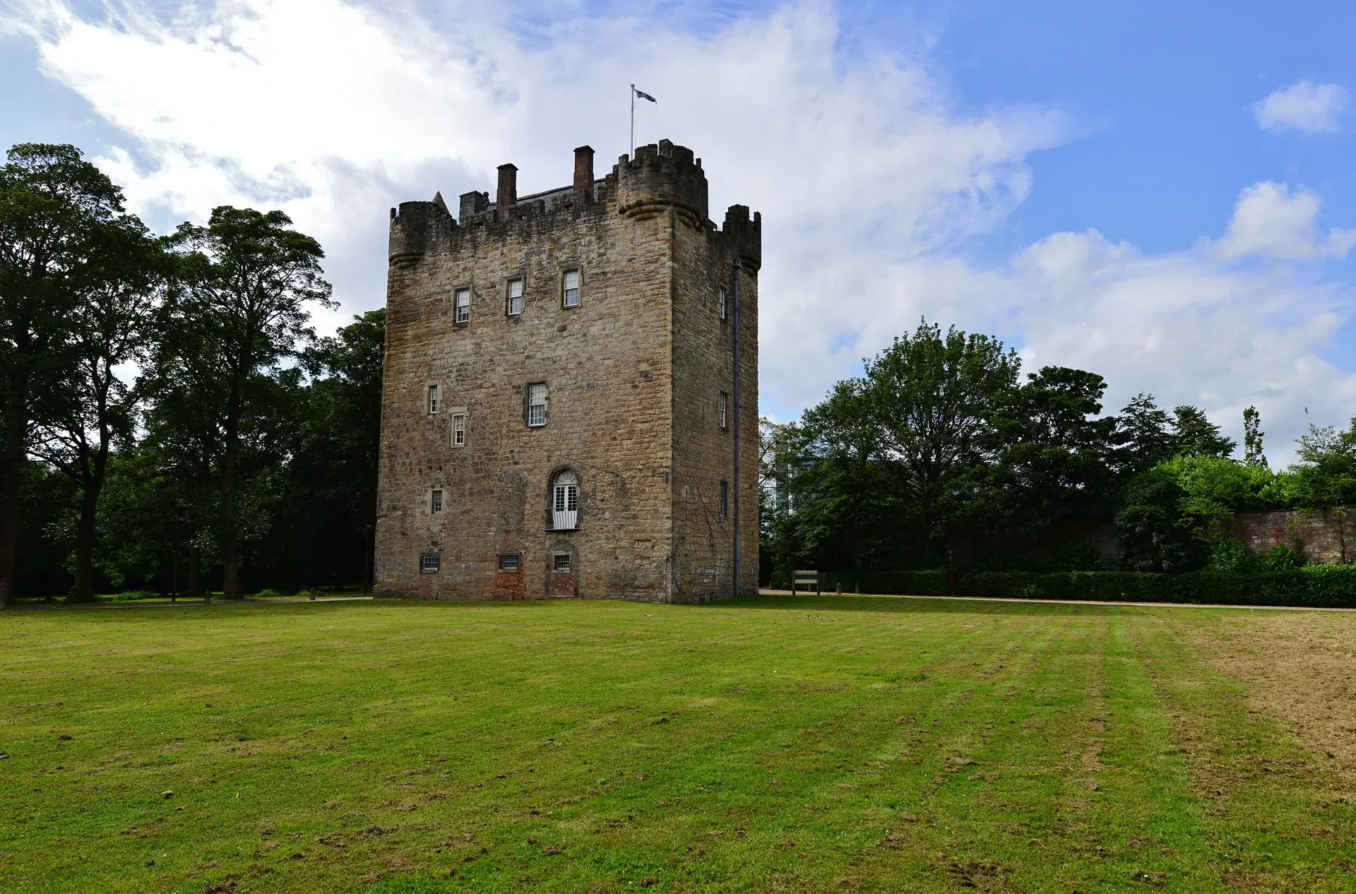 Alloa Tower rising above a green lawn, framed by trees beneath a blue and cloudy sky