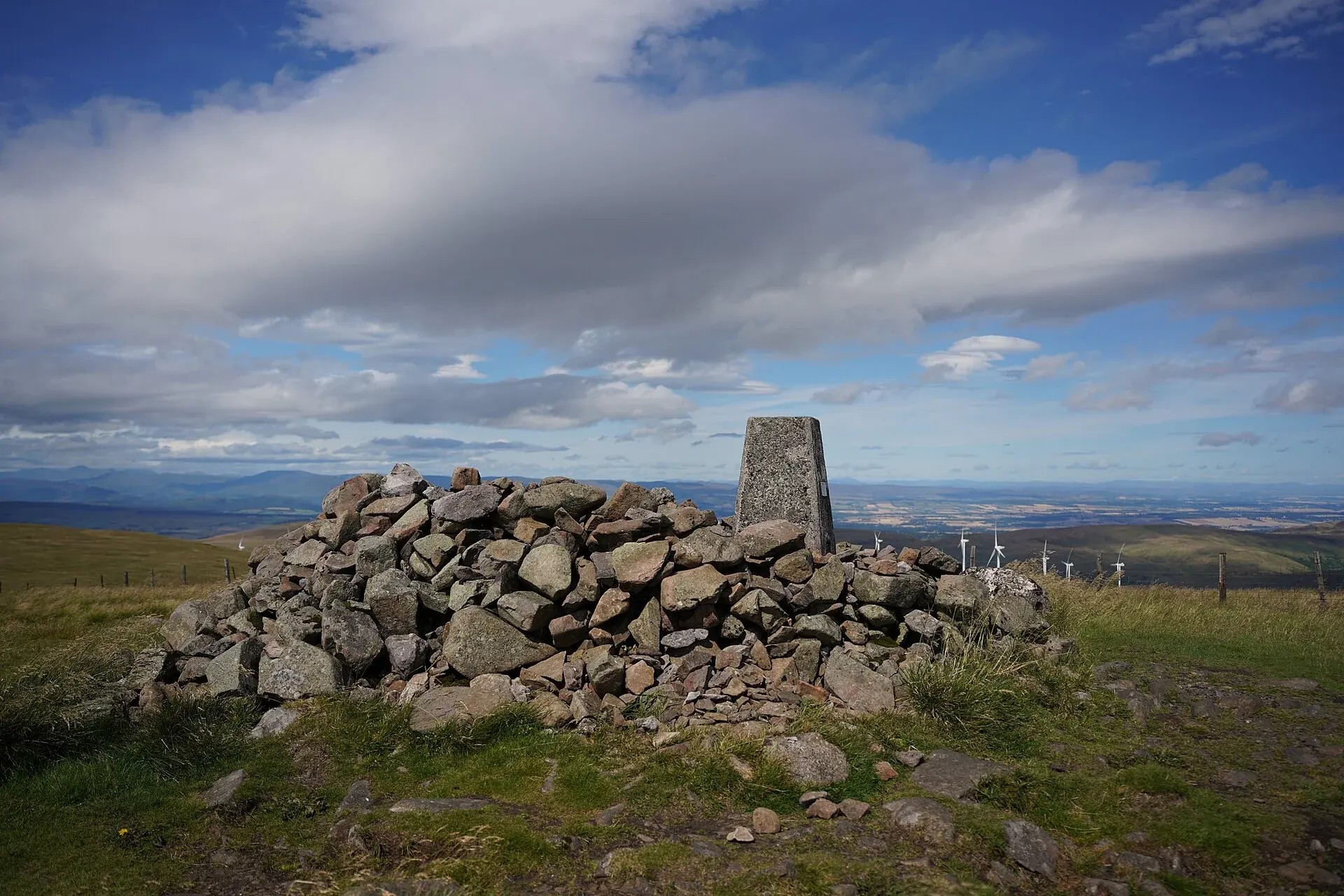 Trig point and stone shelter on Ben Cleuch summit, with a wide view across the Ochil Hills