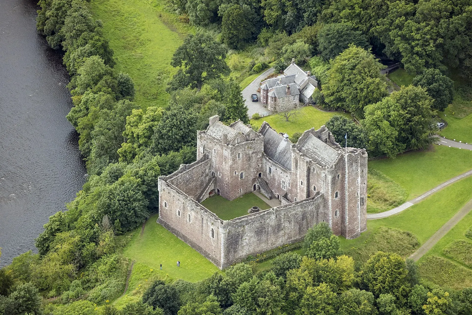 Aerial view of Doune Castle surrounded by green lawns, trees and the River Teith