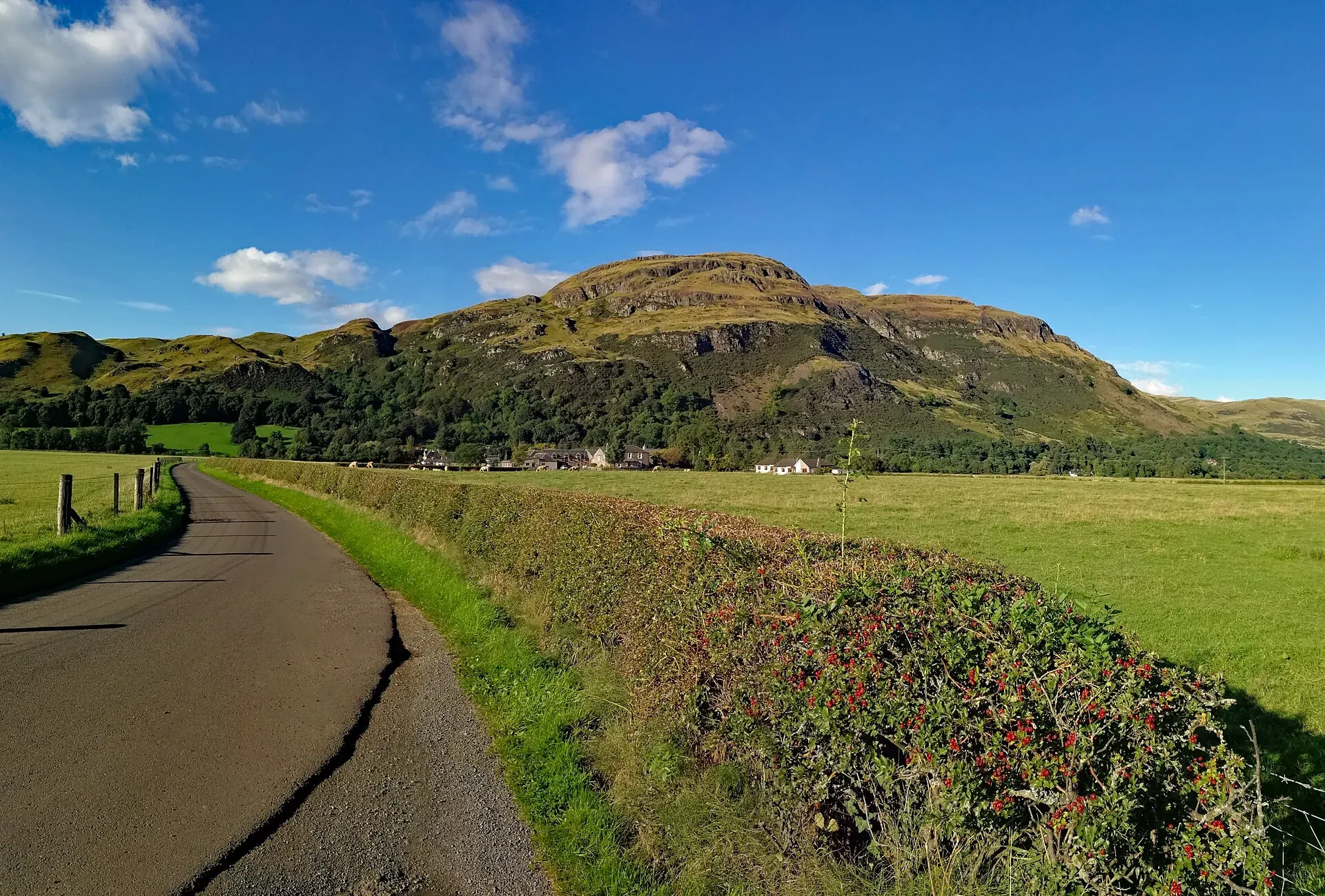 Sunlit slopes of Dumyat above green fields and a country lane near Stirling