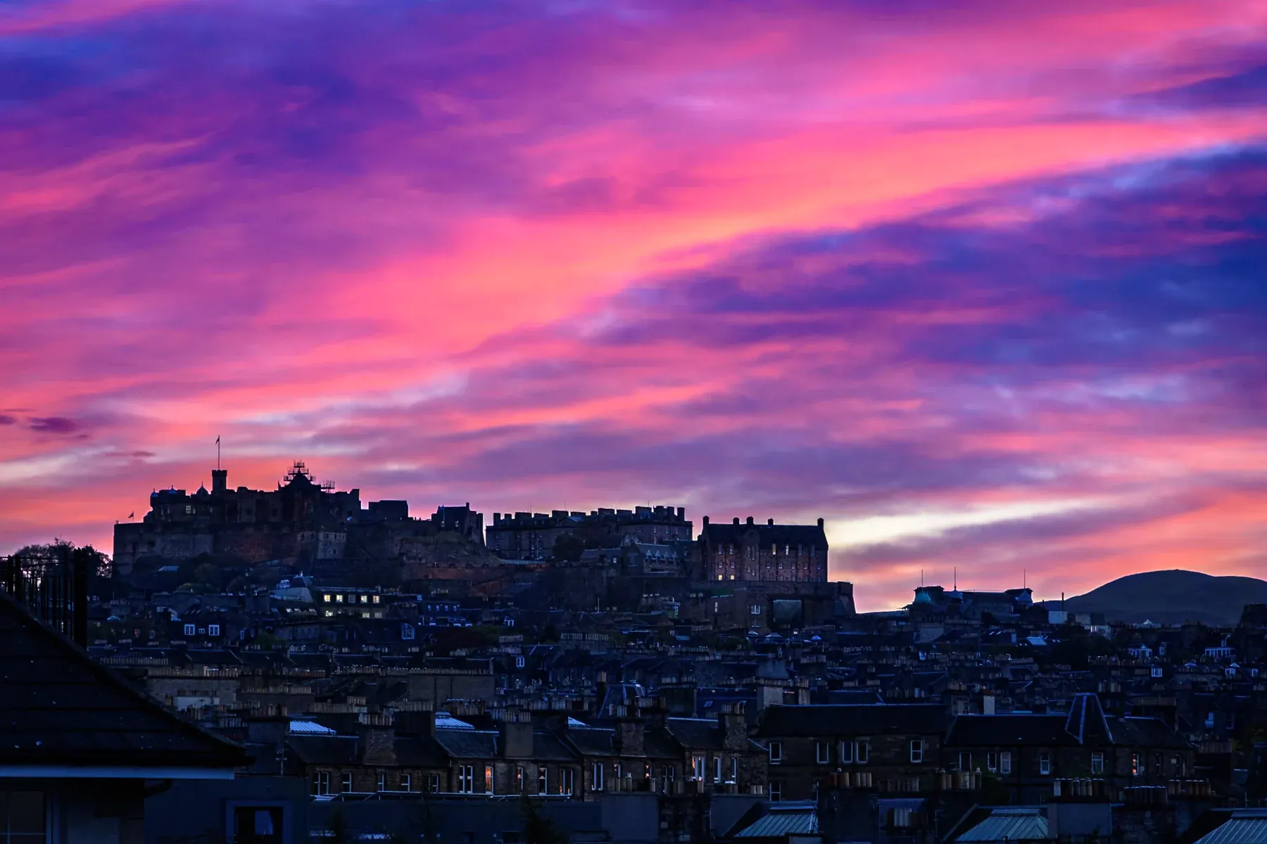Edinburgh Castle above the Old Town rooftops beneath a pink and purple sunset