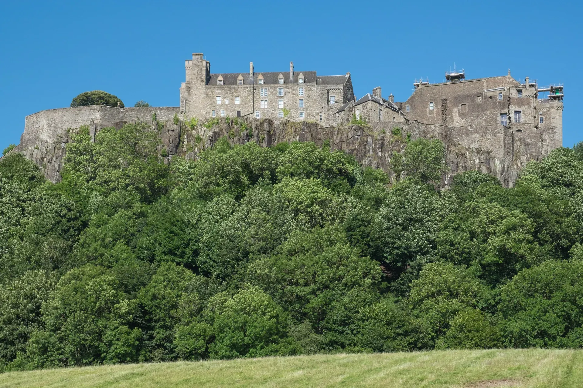 Stirling Castle on its rocky crag above green woodland under a clear blue sky